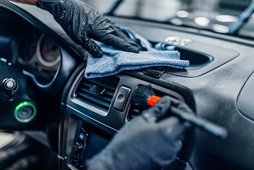 Auto detailing of car interior on carwash service. Worker in gloves cleans salon with brush